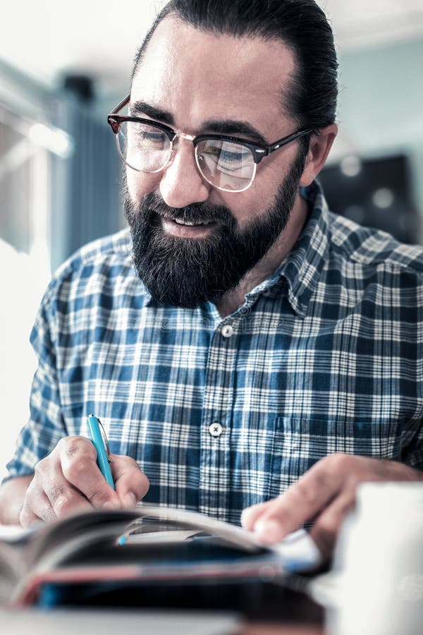 Закройте вверх бородатой темн-с волосами ручки удерживания бизнесмена и примечания делать стоковое изображение