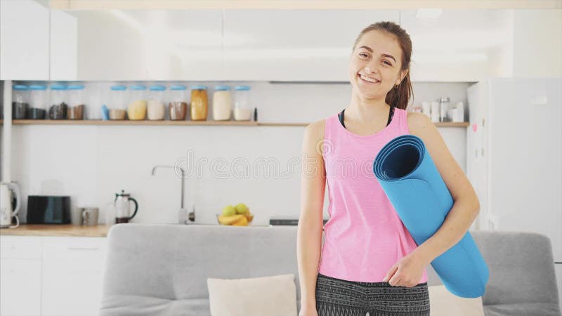 Закройте вверх молодой красивой женщины одетой в голубой jogging или циновки фитнеса после работать дома в живущей комнате