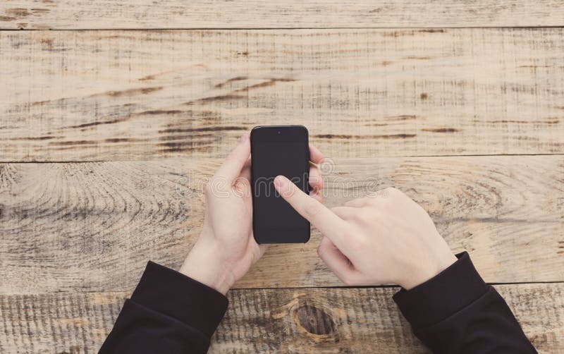 Закройте вверх мужских рук держа smartphone и указывая палец для того чтобы изобразить и отправить СМС на экране на планках табли стоковые изображения rf