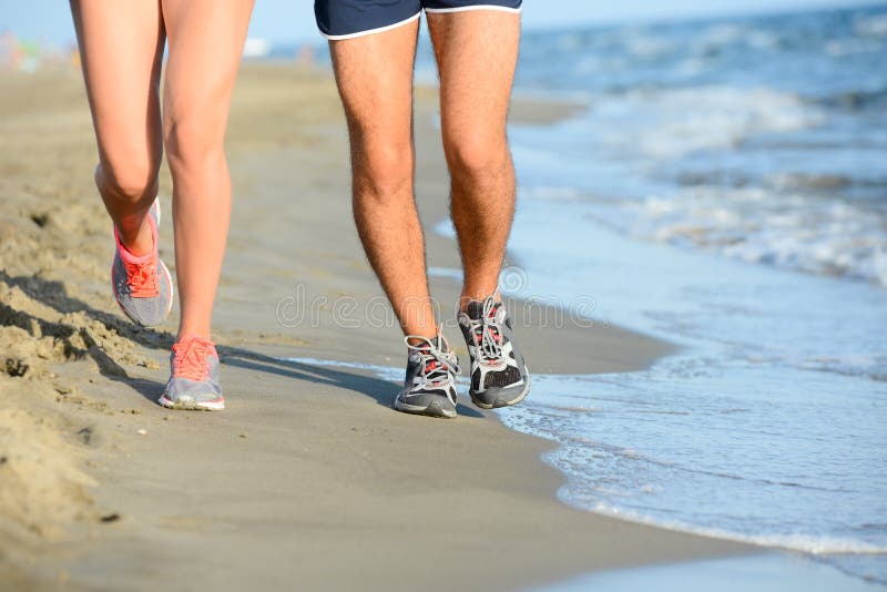 Close up legs of young couple men and women running in the sand on shore of beach by the sea during sunny summer holiday vacation. Close up legs of young couple men and women running in the sand on shore of beach by the sea during sunny summer holiday vacation