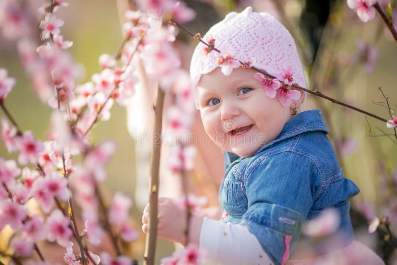 Close-up portrait of a 1-2 year old girl outdoors in a garden with pink flowers in the trees. Close-up portrait of a 1-2 year old girl outdoors in a garden with pink flowers in the trees.