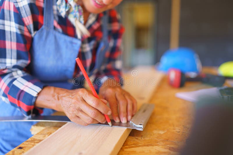 Close up of a senior woman measuring wooden board inside of her unfinished ecological wooden eco house. Close up of a senior woman measuring wooden board inside of her unfinished ecological wooden eco house.