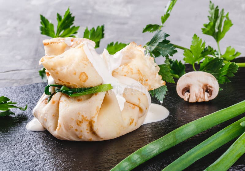 Заполненный крепирует покрытый с соусом и зелеными цветами julienne гриба в плите над темной серой каменной поверхностью Неделя и стоковая фотография rf Заполненный крепирует покрытый с соусом и зелеными цветами julienne гриба в плите над темной серой каменной поверхностью Неделя и стоковая фотография rf
