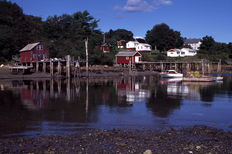 Shoreline reflections in New Harbor, Maine at low tide with red and white structures lining the water's edge and wooden piers jutting into the water. Shoreline reflections in New Harbor, Maine at low tide with red and white structures lining the water's edge and wooden piers jutting into the water.