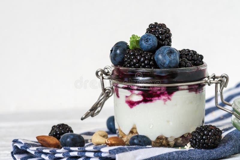 Здоровый югурт ягоды с свежими голубиками, ежевиками, granola, гайками и мятой в опарнике на полотенце кухни стоковое фото rf Здоровый югурт ягоды с свежими голубиками, ежевиками, granola, гайками и мятой в опарнике на полотенце кухни стоковое фото rf