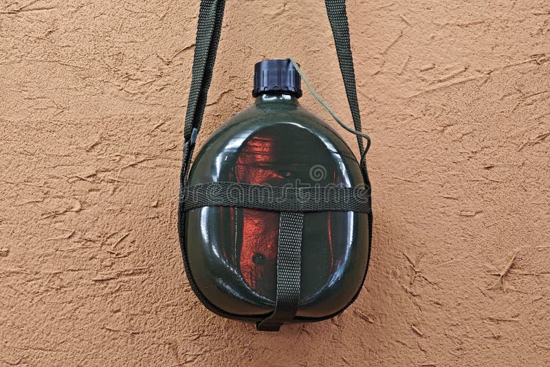 The green old-fashioned military kettle hanging on the yellow mud wall. This kind of kettle was popular in China in the 1960s and 1970s. It was first used in military kettles. Later, it became more common among civilians, but it is now rare. The green old-fashioned military kettle hanging on the yellow mud wall. This kind of kettle was popular in China in the 1960s and 1970s. It was first used in military kettles. Later, it became more common among civilians, but it is now rare.