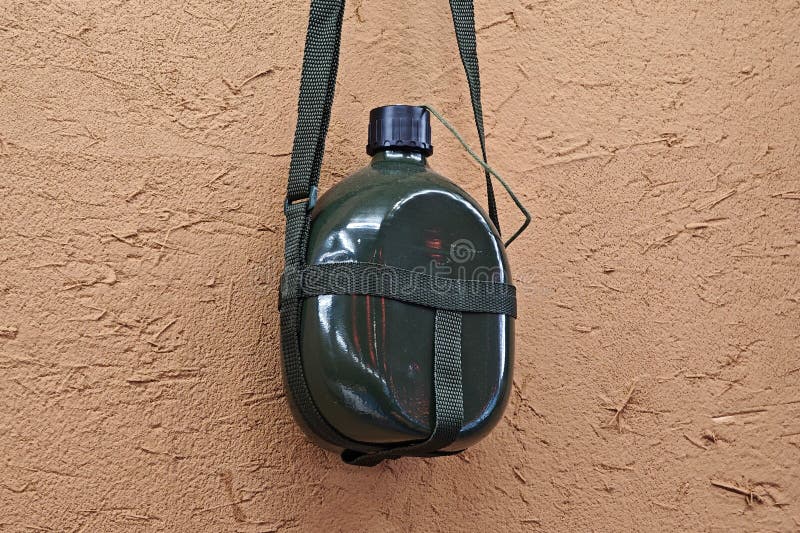 The green old-fashioned military kettle hanging on the yellow mud wall. This kind of kettle was popular in China in the 1960s and 1970s. It was first used in military kettles. Later, it became more common among civilians, but it is now rare. The green old-fashioned military kettle hanging on the yellow mud wall. This kind of kettle was popular in China in the 1960s and 1970s. It was first used in military kettles. Later, it became more common among civilians, but it is now rare.