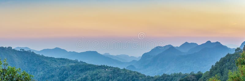 Знамя сети природы Взгляд панорамы захода солнца горного вида много холм и зеленая крышка леса с мягким туманом с красочным небом