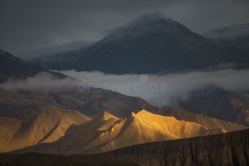 Beautiful natural scenery. Hills brightly lit by the sunlight with dramatic mountain view on the backside. Captured in Upper Mustang region, Himalayas, Nepal. Beautiful natural scenery. Hills brightly lit by the sunlight with dramatic mountain view on the backside. Captured in Upper Mustang region, Himalayas, Nepal.