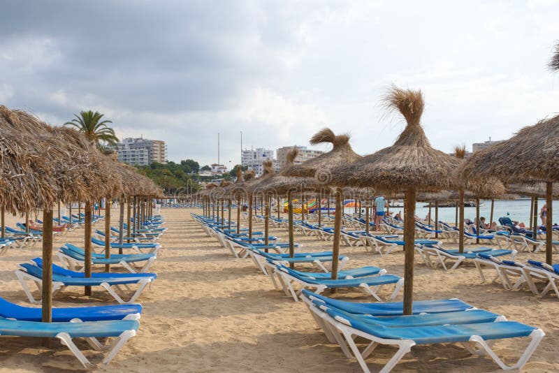Зонтики Мальорка традиционные покрыванные соломой и голубые sunbeds на песчаном пляже курорта Magaluf E стоковая фотография rf