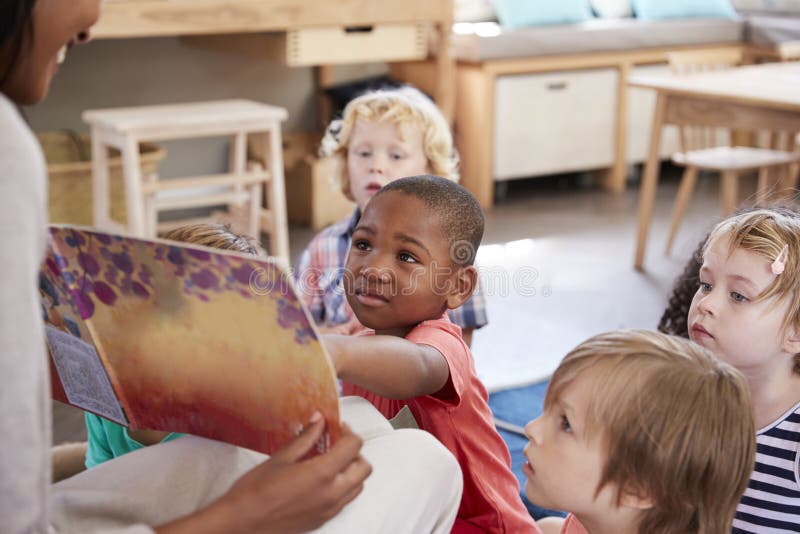 Зрачки на школе Montessori смотря книгу с учителем стоковые фотографии rf Зрачки на школе Montessori смотря книгу с учителем стоковые фотографии rf