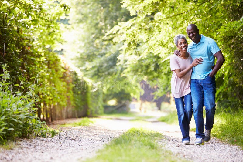 Mature African American Couple Walking In Countryside With Arms Around Each Other Smiling. Mature African American Couple Walking In Countryside With Arms Around Each Other Smiling