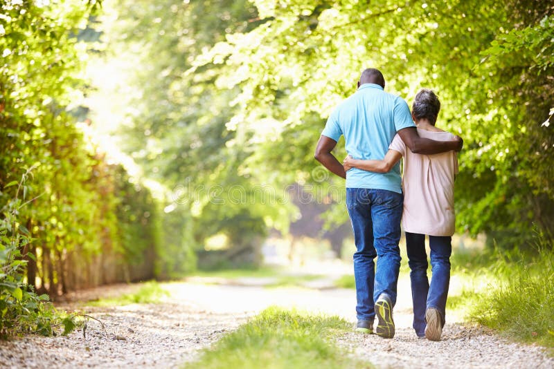 Mature African American Couple Walking In Countryside Away From Camera With Arms Around Each Other. Mature African American Couple Walking In Countryside Away From Camera With Arms Around Each Other