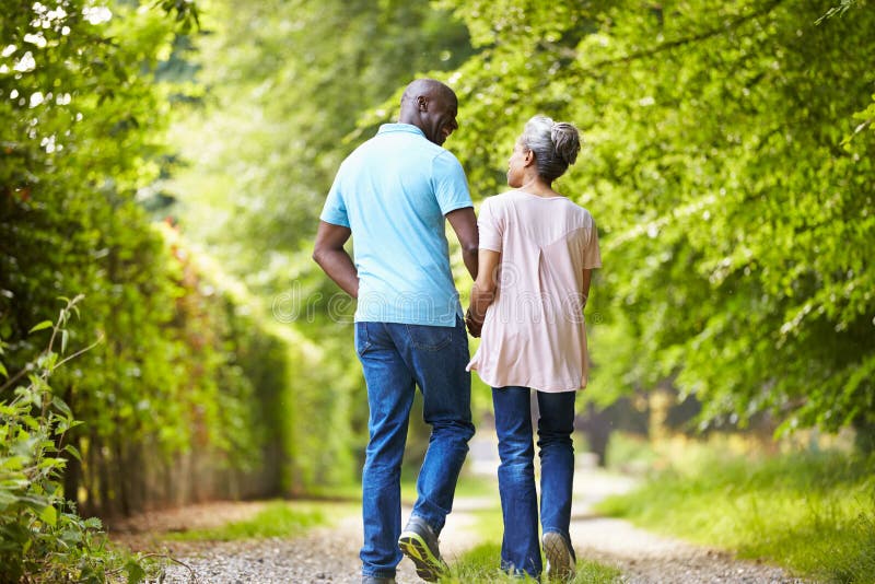 Mature African American Couple Walking In Countryside Holding Hands Smiling At Each Other. Mature African American Couple Walking In Countryside Holding Hands Smiling At Each Other