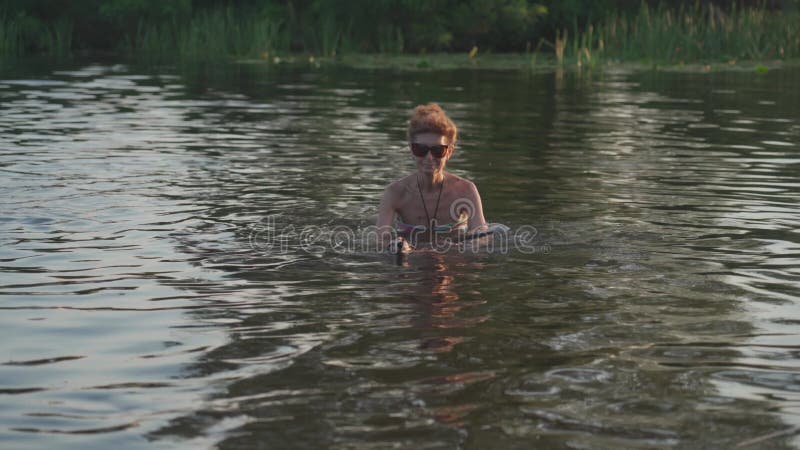 зрелая женщина с маленькой старой собачкой плавают в воде. пожилая самка проводит лето на реке со своей собакой. день отпуска видеоматериал