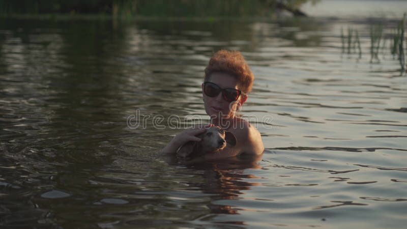 зрелая женщина с маленькой старой собачкой плавают в воде. пожилая самка проводит лето на реке со своей собакой. день отпуска акции видеоматериалы