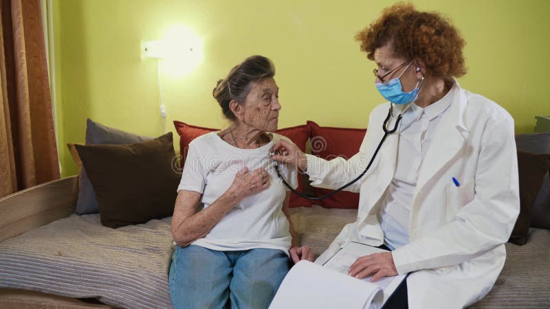 Зрелые женщины, занимающих стетоскоп с учетом старший врач пациента бабушки дома. Женщина в возрасте слушает врач сток-видео