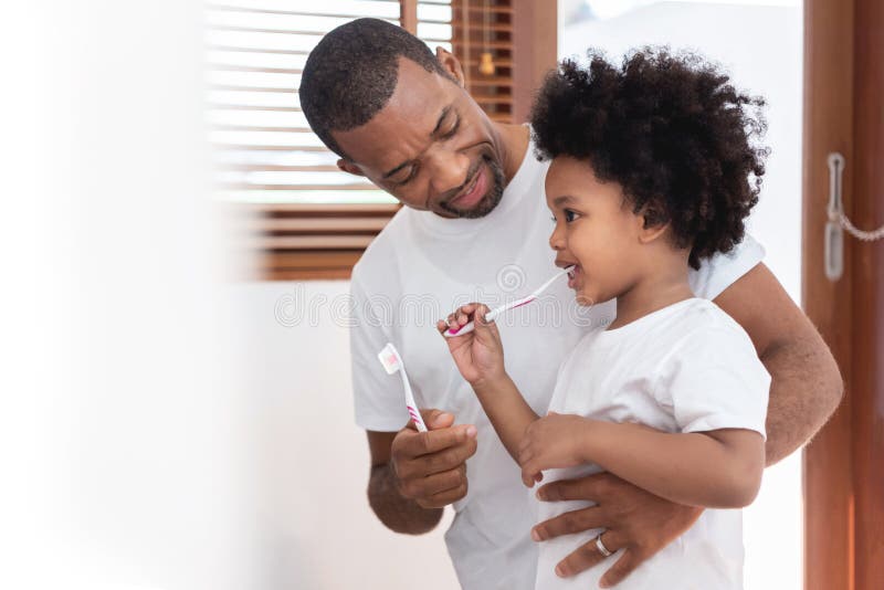 Happy African American Family, Dad teaching his son in white shirts brushing teeth in bathroom together. Father and kid boy in curly hair enjoying with dental hygiene at home in morning. Happy African American Family, Dad teaching his son in white shirts brushing teeth in bathroom together. Father and kid boy in curly hair enjoying with dental hygiene at home in morning