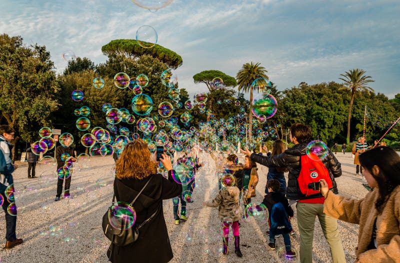 Rome / Italy - December 2 2018: The children play and try to catch the soap bubbles while the adults take photos, at Terrazza del Pincio. Rome / Italy - December 2 2018: The children play and try to catch the soap bubbles while the adults take photos, at Terrazza del Pincio.