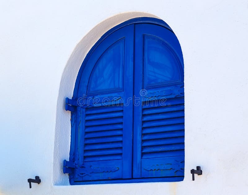 Известное округленное голубое деревянное окно на белой стене, Santorini, Греции стоковая фотография rf Известное округленное голубое деревянное окно на белой стене, Santorini, Греции стоковая фотография rf