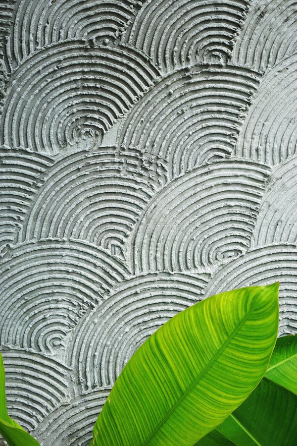 Overlapping grooved concentric circles cover an exterior wall in Vietnam. Bright green tropical leaves at the bottom edge. Overlapping grooved concentric circles cover an exterior wall in Vietnam. Bright green tropical leaves at the bottom edge.