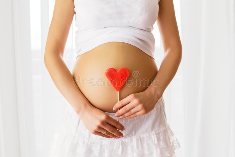 Picture of pregnant woman holding heart sign to her belly. Picture of pregnant woman holding heart sign to her belly