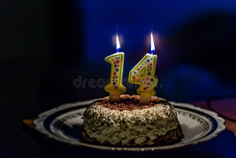 Cream and chocolate cake with lit number one and number four candles to celebrate fourteen years birthday in dark blurred background. Cream and chocolate cake with lit number one and number four candles to celebrate fourteen years birthday in dark blurred background
