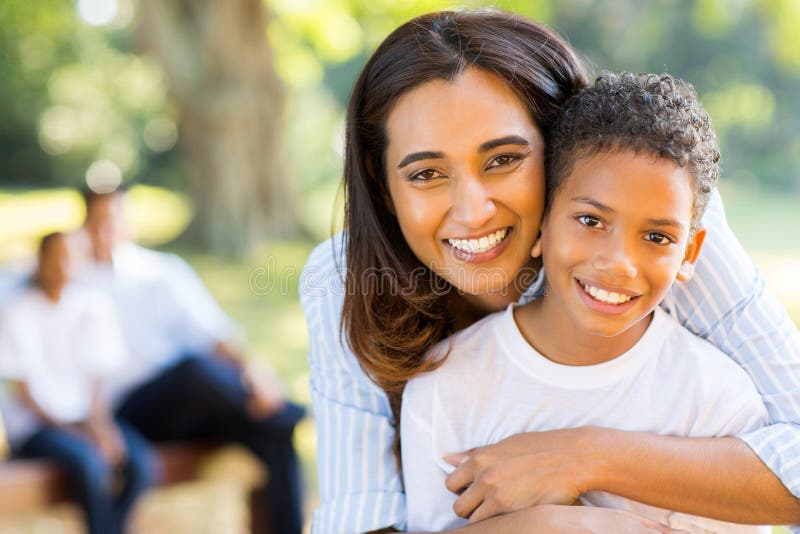 Happy indian mother hugging her son in front of family outdoors. Happy indian mother hugging her son in front of family outdoors