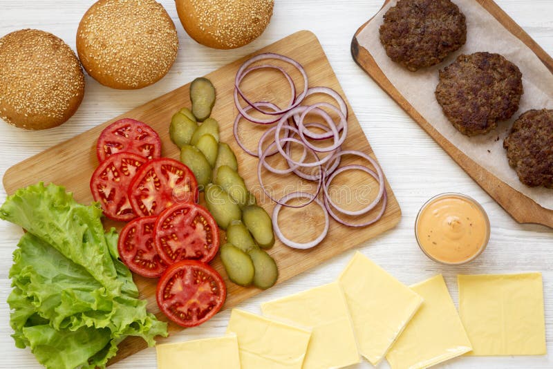 Ингредиенты Cheeseburger на белой деревянной предпосылке, взгляде сверху r closeup стоковое фото rf