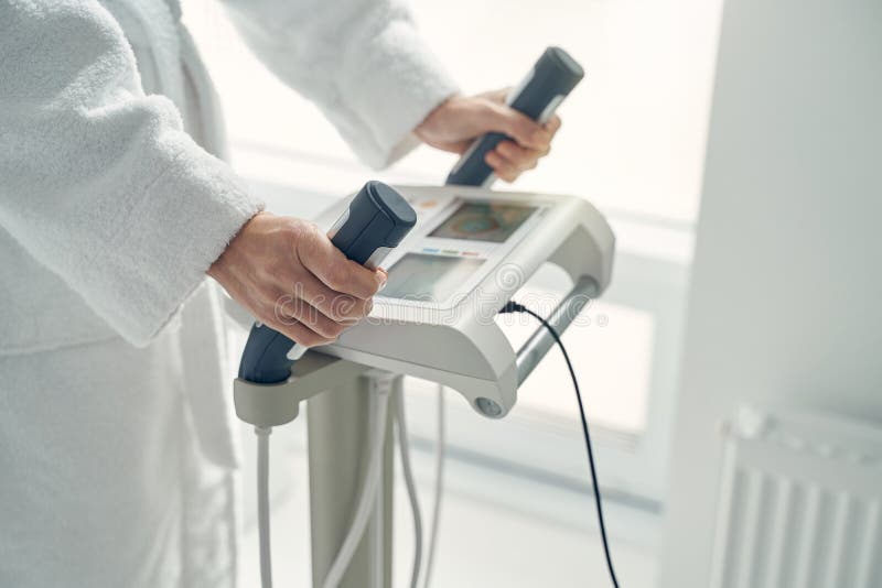 Mature woman in white bathrobe using high technology medical tool while following health changes with handles in hands. Mature woman in white bathrobe using high technology medical tool while following health changes with handles in hands