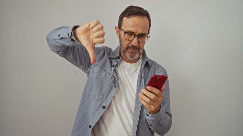 Испаноязычный мужчина среднего возраста с помощью смартфона с большим пальцем вниз знак показывая негативную неприязнь и неприятие сток-видео