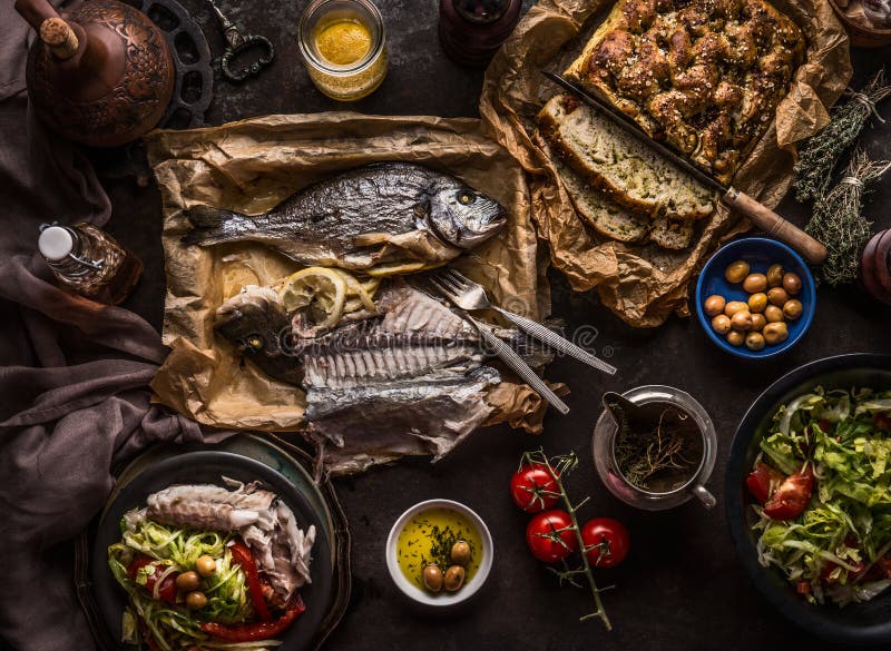 Испеченные рыбы dorado на темной таблице с салатницей, хлебом focaccia, томатами и оливками, взглядом сверху Среднеземноморские о стоковая фотография Испеченные рыбы dorado на темной таблице с салатницей, хлебом focaccia, томатами и оливками, взглядом сверху Среднеземноморские о стоковая фотография