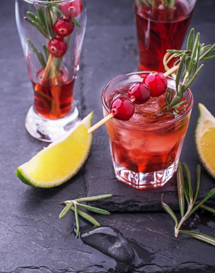 Bright festive cranberry cocktail with frozen cranberries on skewers and a sprig of fresh rosemary in glass glasses on a black stone plaque. selective Focus. Bright festive cranberry cocktail with frozen cranberries on skewers and a sprig of fresh rosemary in glass glasses on a black stone plaque. selective Focus