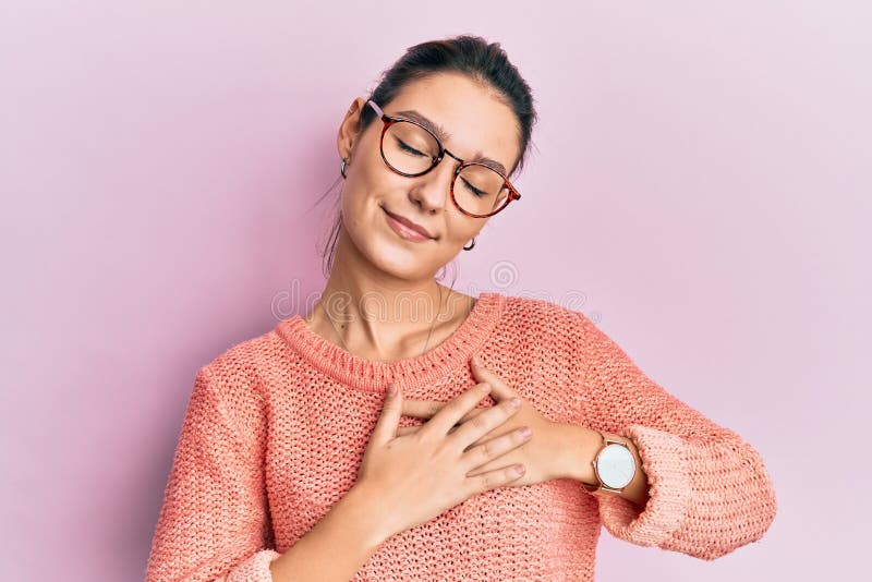 Young caucasian woman wearing casual clothes and glasses smiling with hands on chest with closed eyes and grateful gesture on face. health concept. Young caucasian woman wearing casual clothes and glasses smiling with hands on chest with closed eyes and grateful gesture on face. health concept