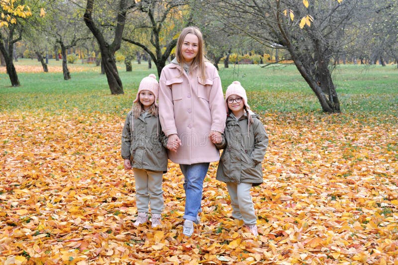 Caucasian family play in autumn park, mother embrace two girls twins and smile, active weekend outdoors. Horizontal photo. Caucasian family play in autumn park, mother embrace two girls twins and smile, active weekend outdoors. Horizontal photo