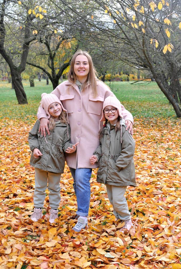 Caucasian family play in autumn park, mother embrace two girls twins and smile, active weekend outdoors. Vertical photo. Caucasian family play in autumn park, mother embrace two girls twins and smile, active weekend outdoors. Vertical photo