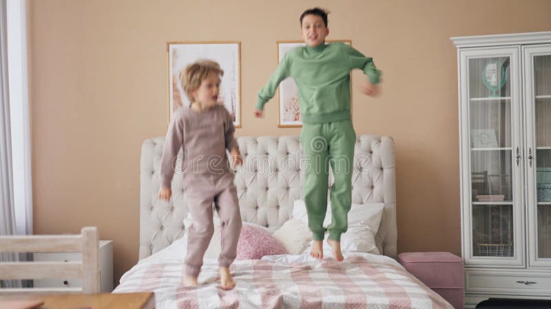 2 Кавказских мальчика, вскочив на кровать, весело смеясь, играя забавную активную игру с прекрасным сыном ребенка в спальне.