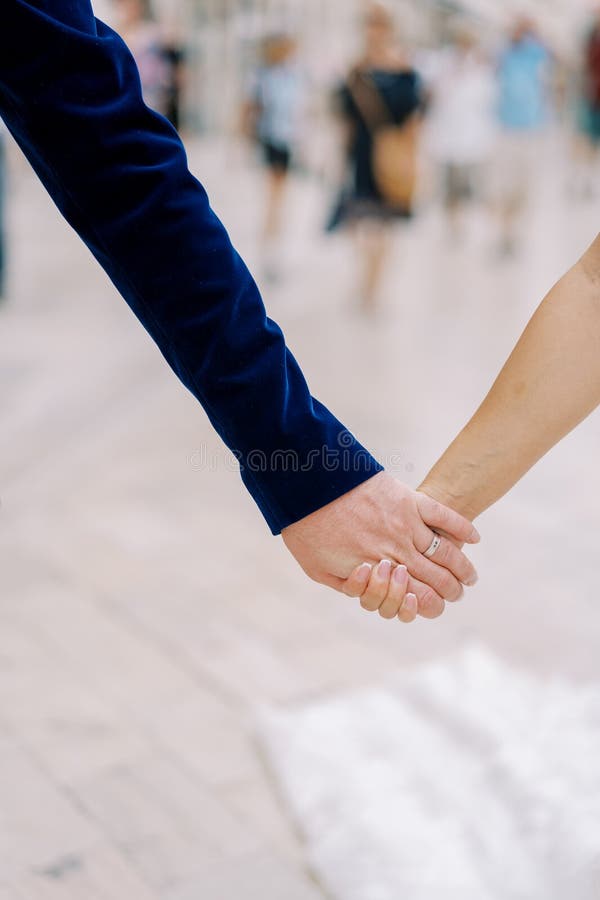 Groom holds bride hand while standing on the street. Cropped. Faceless. High quality photo. Groom holds bride hand while standing on the street. Cropped. Faceless. High quality photo