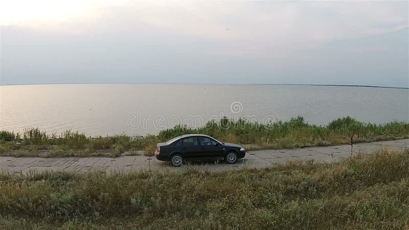 Камера на трутне отслеживает автомобиль, который едет вдоль обваловки около моря