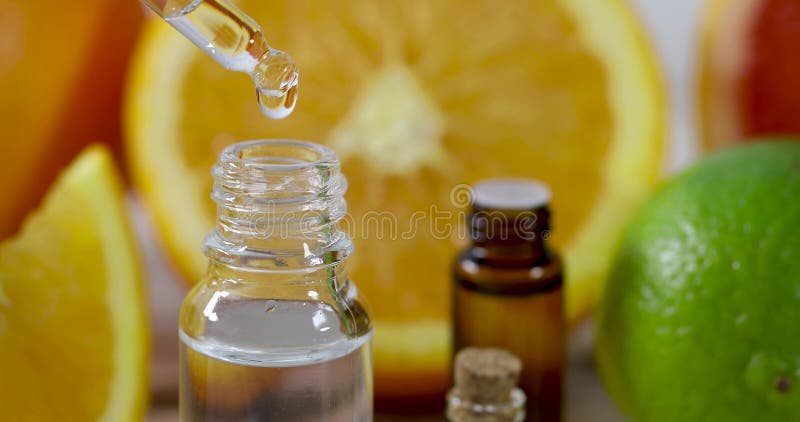 Капание эфирного масла цитруса от пипетки на предпосылке свежих фруктов
