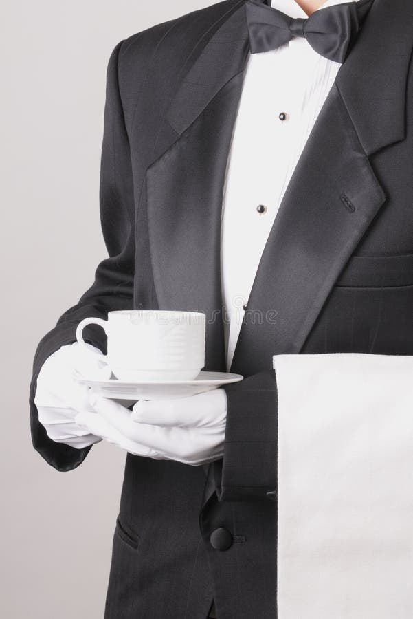 Waiter in Tuxedo holding a coffee cup with a towel draped over his arm torso only vertical format over gray background. Waiter in Tuxedo holding a coffee cup with a towel draped over his arm torso only vertical format over gray background