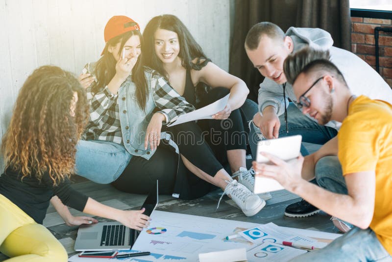 Millennials business routine. Young people cooperating in modern loft office, sitting on floor. Positive working climate. Millennials business routine. Young people cooperating in modern loft office, sitting on floor. Positive working climate.