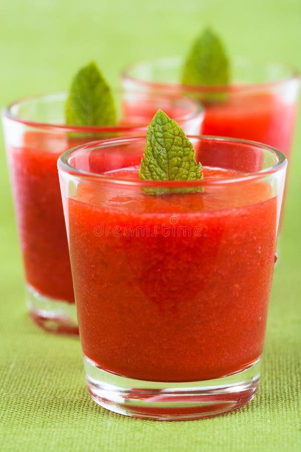 Three little glasses of strawberry smoothie on a green background. Three little glasses of strawberry smoothie on a green background
