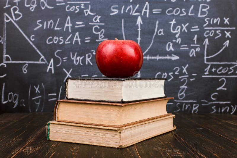 Книги и яблоко на деревянном столе, на фоне доски с формулами Teacher& x27; концепция дня s и назад к стоковое изображение rf Книги и яблоко на деревянном столе, на фоне доски с формулами Teacher& x27; концепция дня s и назад к стоковое изображение rf