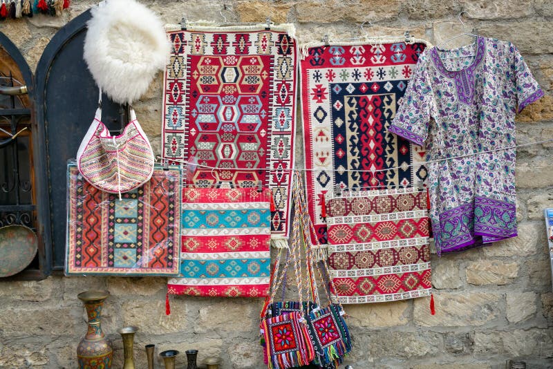 Ковры, сумки, куртка handmade с национальными печатями, белая крышка шерстей овец вися на предпосылке старой каменной стены стоковые изображения Ковры, сумки, куртка handmade с национальными печатями, белая крышка шерстей овец вися на предпосылке старой каменной стены стоковые изображения