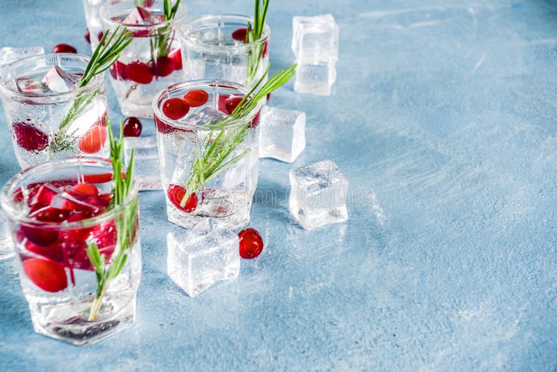 Christmas or New Year winter cranberry cocktail with rosemary, liqueur, gin tonic, on light blue concrete background with ice cubes, fresh berries and rosemary twig copy space. Christmas or New Year winter cranberry cocktail with rosemary, liqueur, gin tonic, on light blue concrete background with ice cubes, fresh berries and rosemary twig copy space