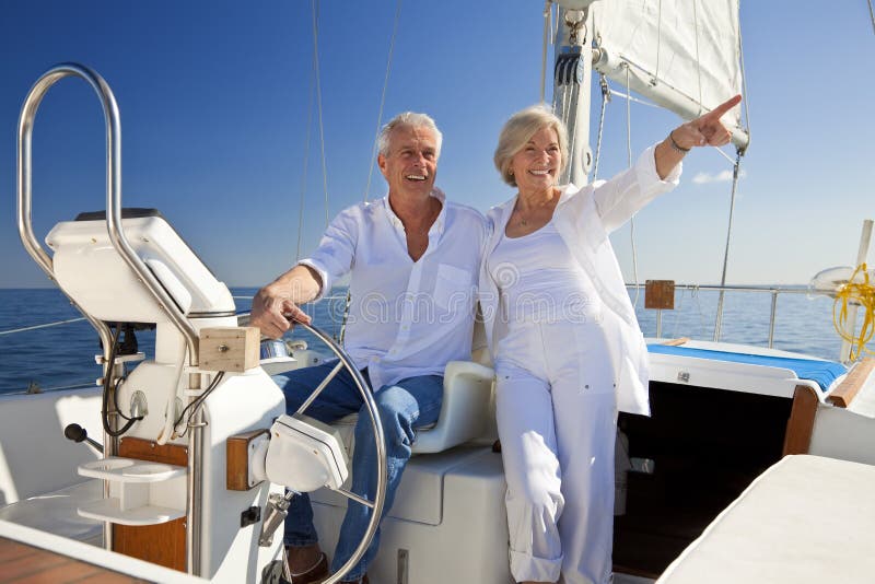 A happy senior couple sitting at the wheel of a sail boat on a calm blue sea. A happy senior couple sitting at the wheel of a sail boat on a calm blue sea