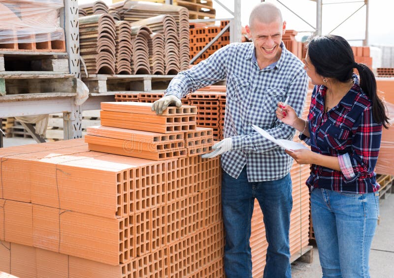 Colleagues man and woman collecting order of red bricks at warehouse of building materials. Colleagues man and woman collecting order of red bricks at warehouse of building materials