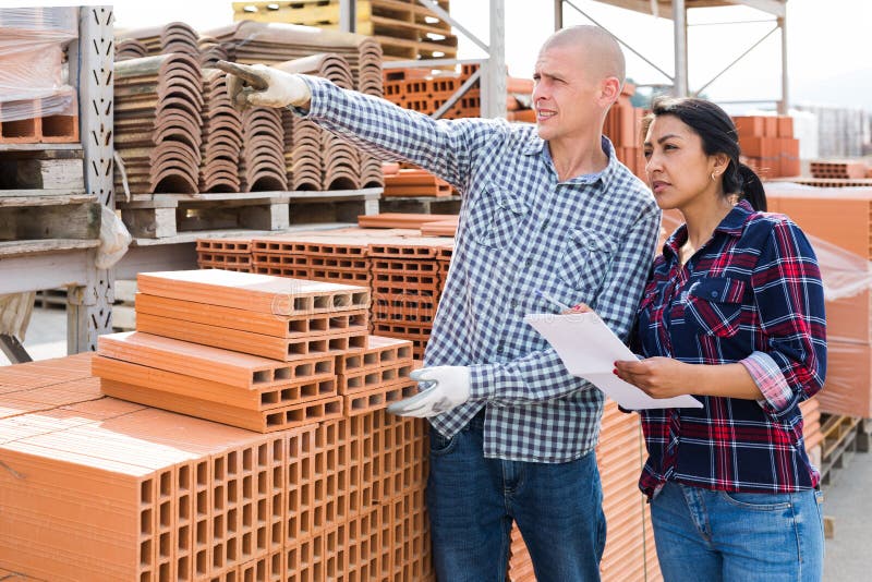 Colleagues men and women collecting order of red bricks at warehouse of building materials. Colleagues men and women collecting order of red bricks at warehouse of building materials