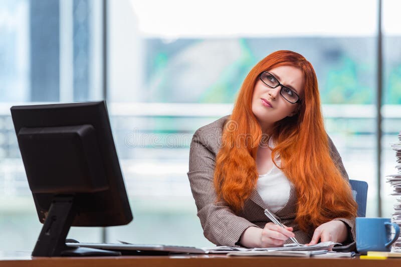 Коммерсантка redhead сидя на ее столе в офисе стоковые фотографии rf Коммерсантка redhead сидя на ее столе в офисе стоковые фотографии rf